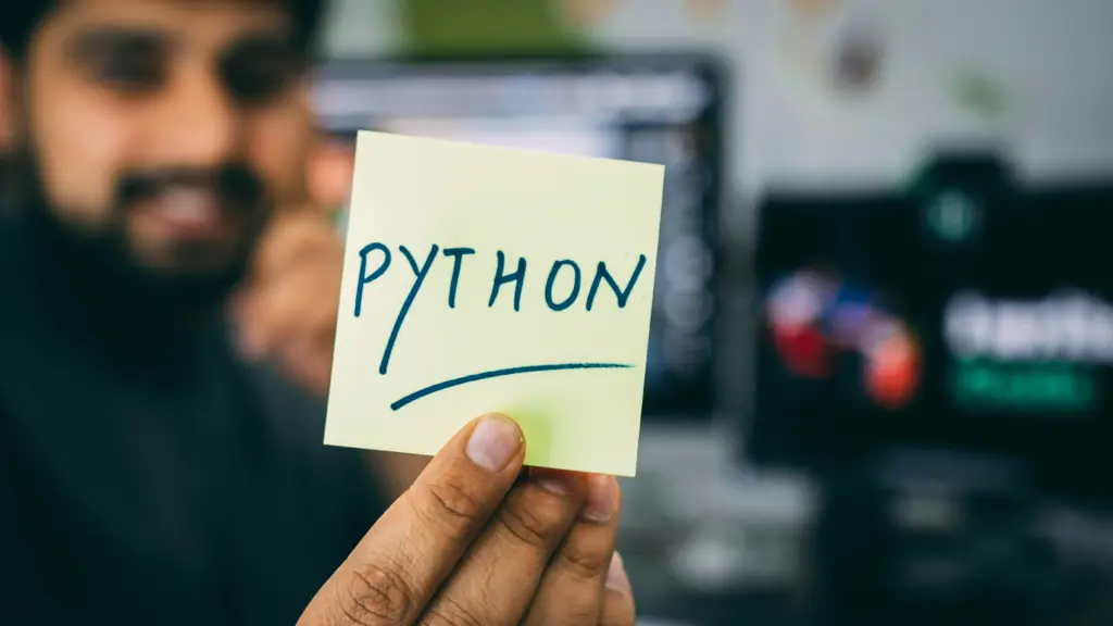 Close up of a man holding a sticky note with the words "Python".