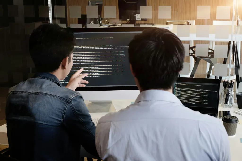 Two men staring at a computer screen with java code.