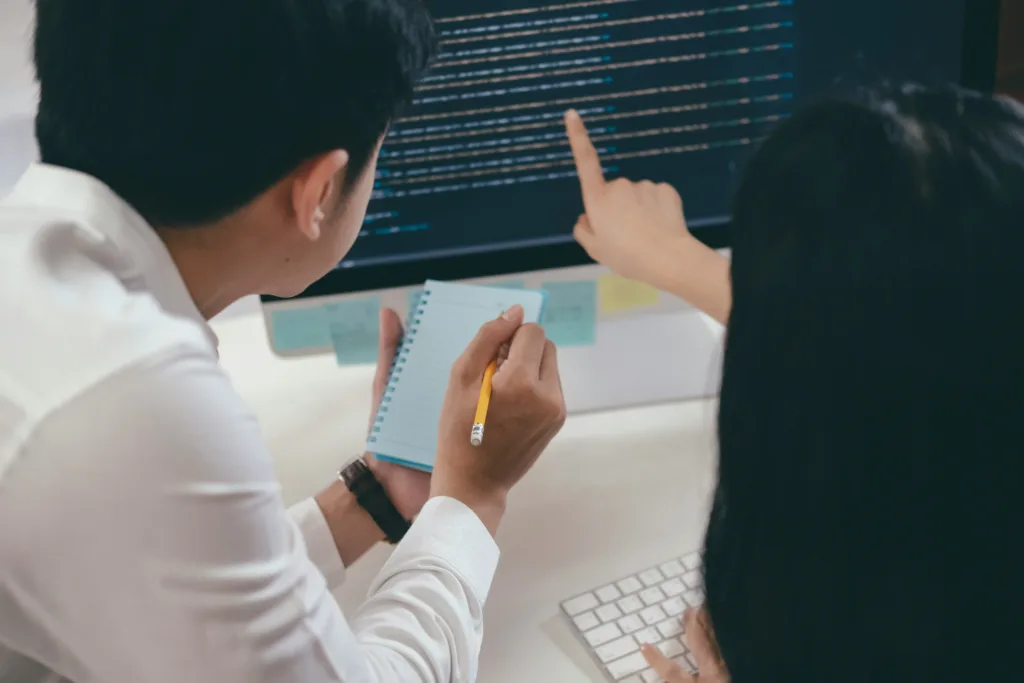 A dark haired man and woman pointing to a computer screen with java on it.