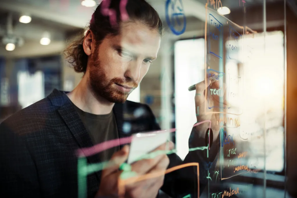 A man writing on a clear whiteboard.