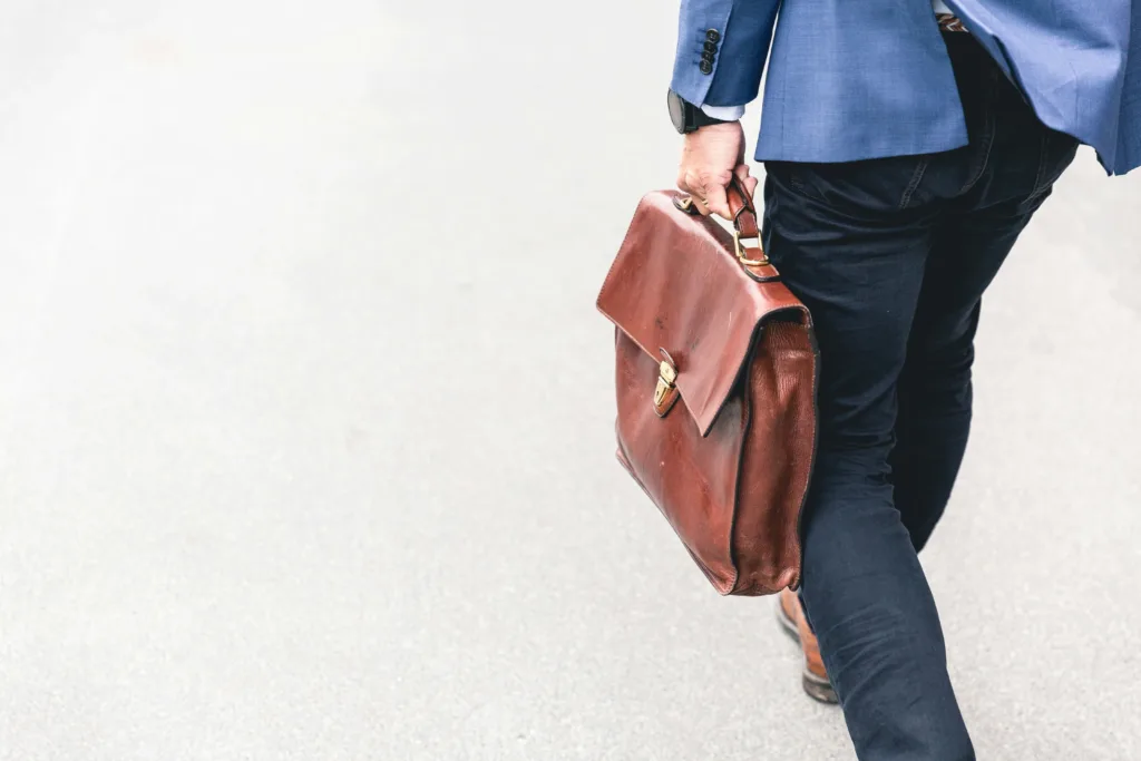 A man walking with a brown briefcase to get hired after taking a C# boot camp.